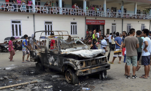 People gather near a damaged vehicle after it was set on fire during a protest in Manipur (Photo: AP) People gather near a damaged vehicle after it was set on fire during a protest in Manipur (Photo: AP)